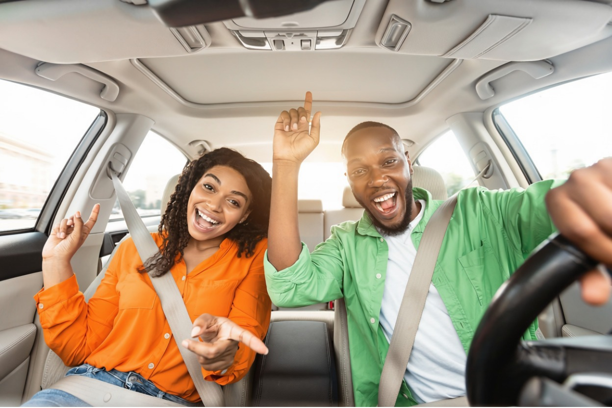 man and woman sit in a parked car raising their hands in excitement.